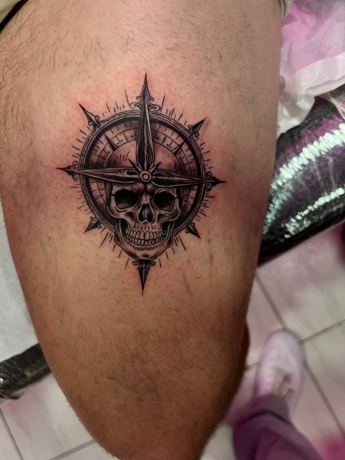 It is a realistic black & grey tattoo with ornamental influence, where a human skull appears fused with a nautical compass. The composition is symmetrical, with sharp points that mark